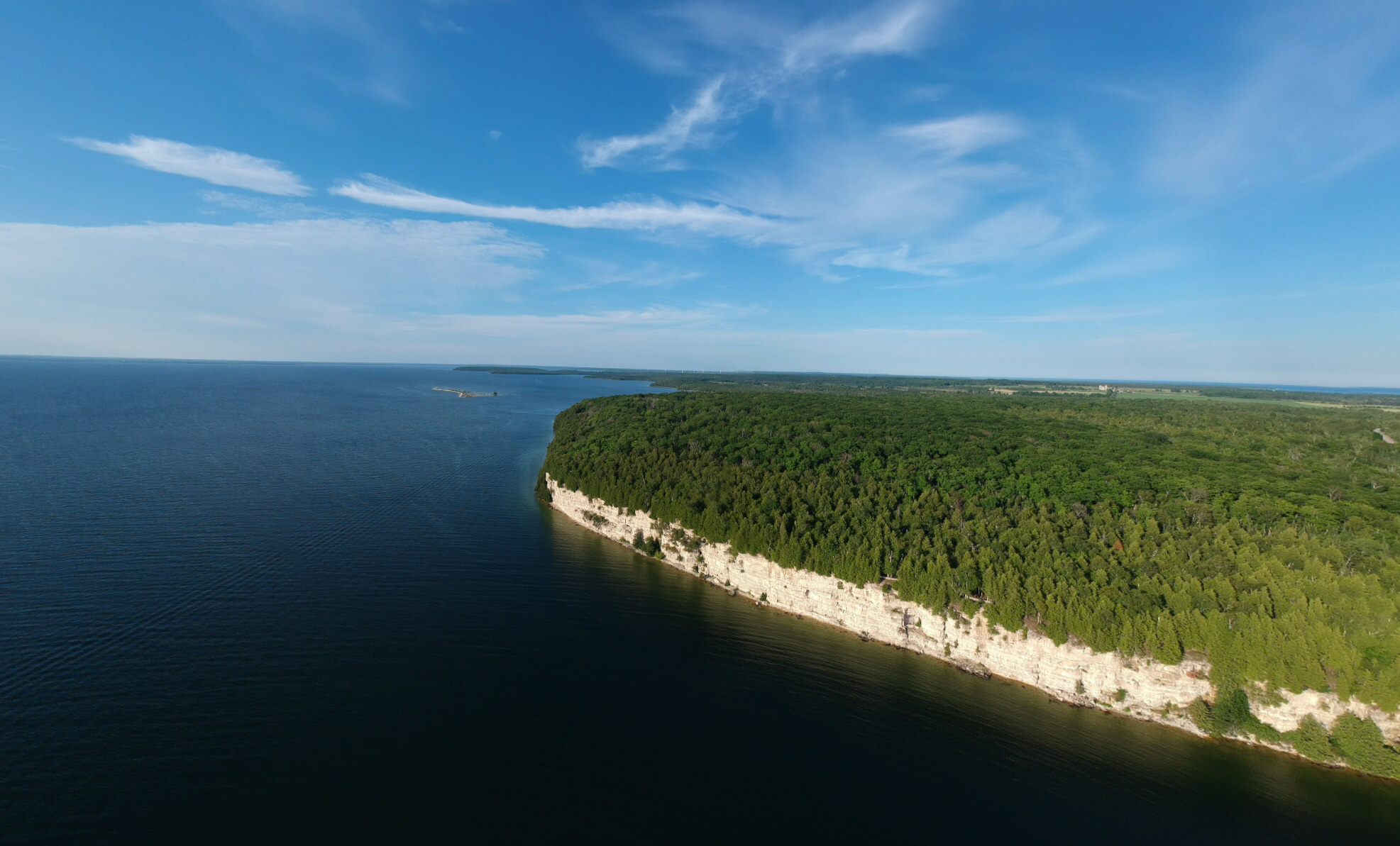 Aerial view of a pale cliff, dense forest, and blue water