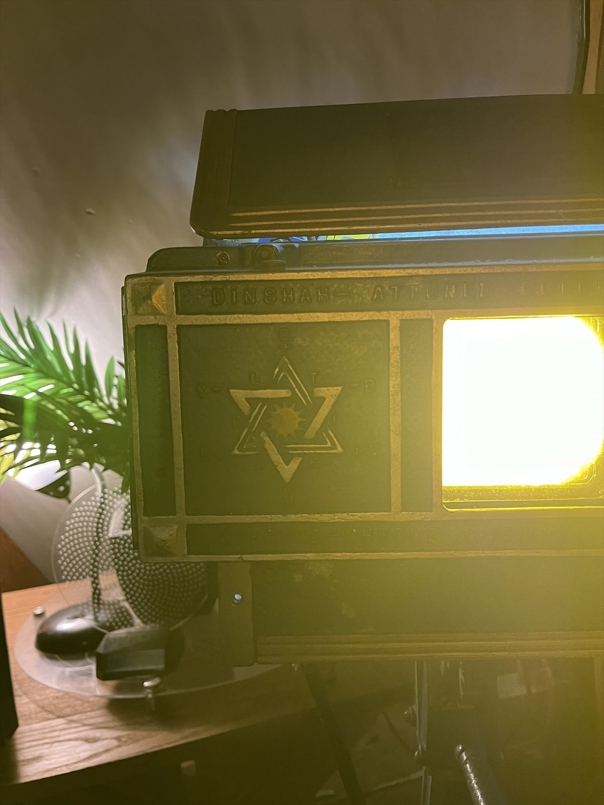 Close view of the same vintage Spectro-Chrome projector glowing yellow, showing its cast-metal face, central emblem, and light aperture.
