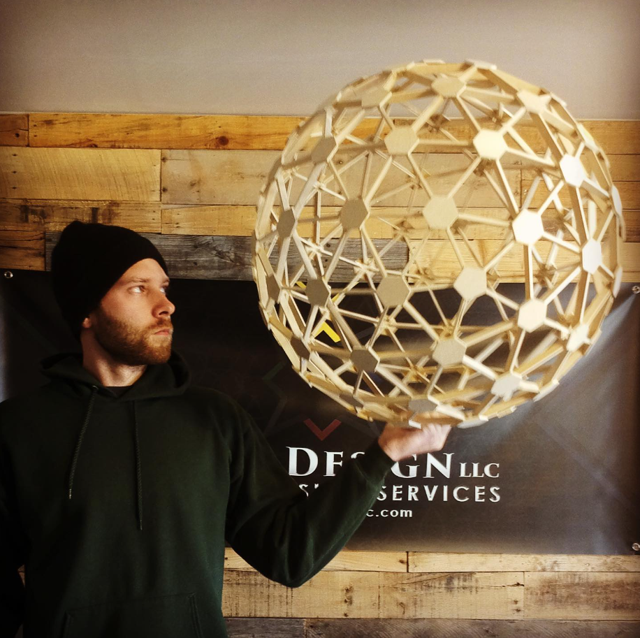 Ryan Nagy holding a handcrafted wooden geodesic sphere in his studio.