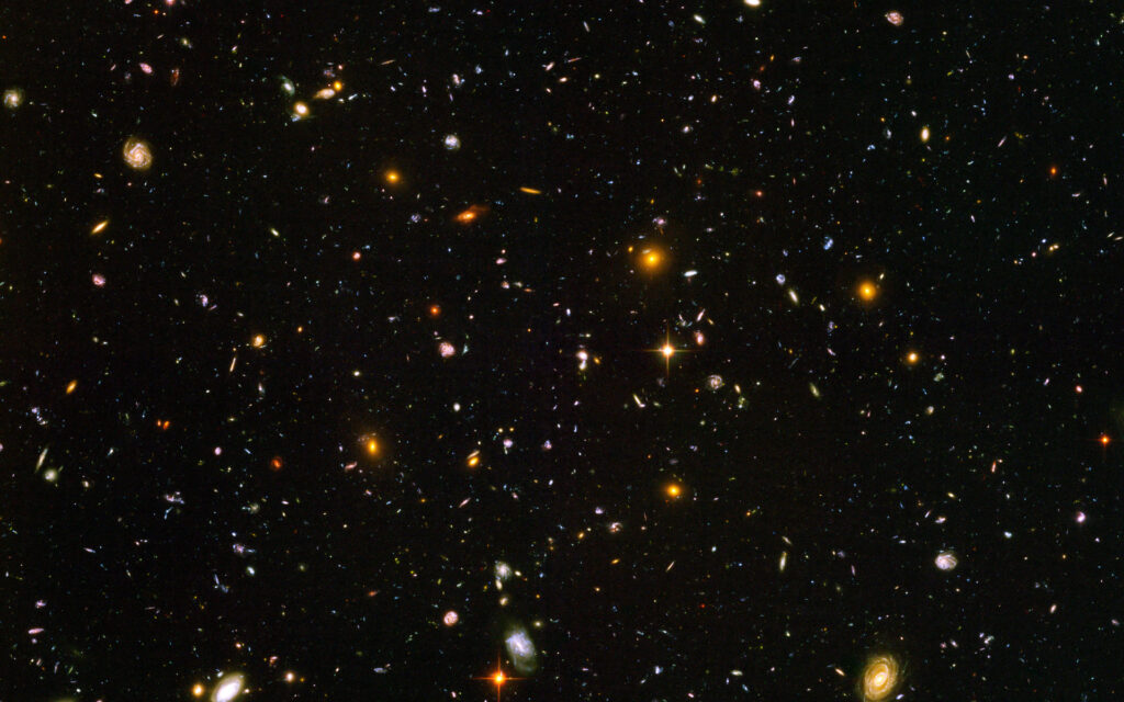 Hubble Ultra Deep Field: scattered spiral and elliptical galaxies, faint red galaxies and a few foreground stars against dark space.